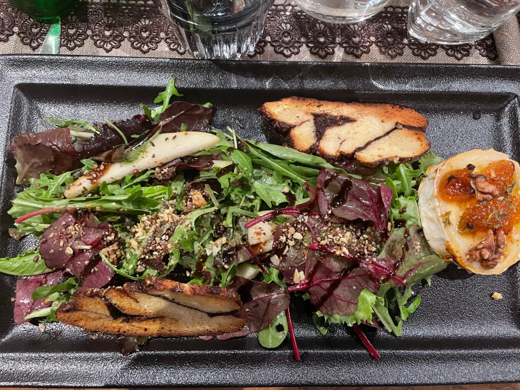 Depicts a leafy salad with goat cheese and nuts.