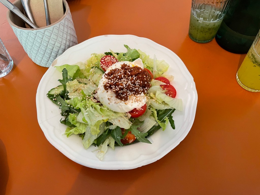 A green salad with mozzarella cheese on top, served in a cracked plate. 