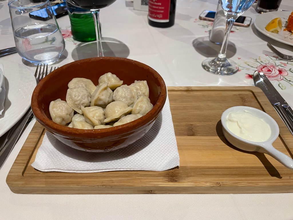 A picture of pelmeni on a board and with sour cream next to them.