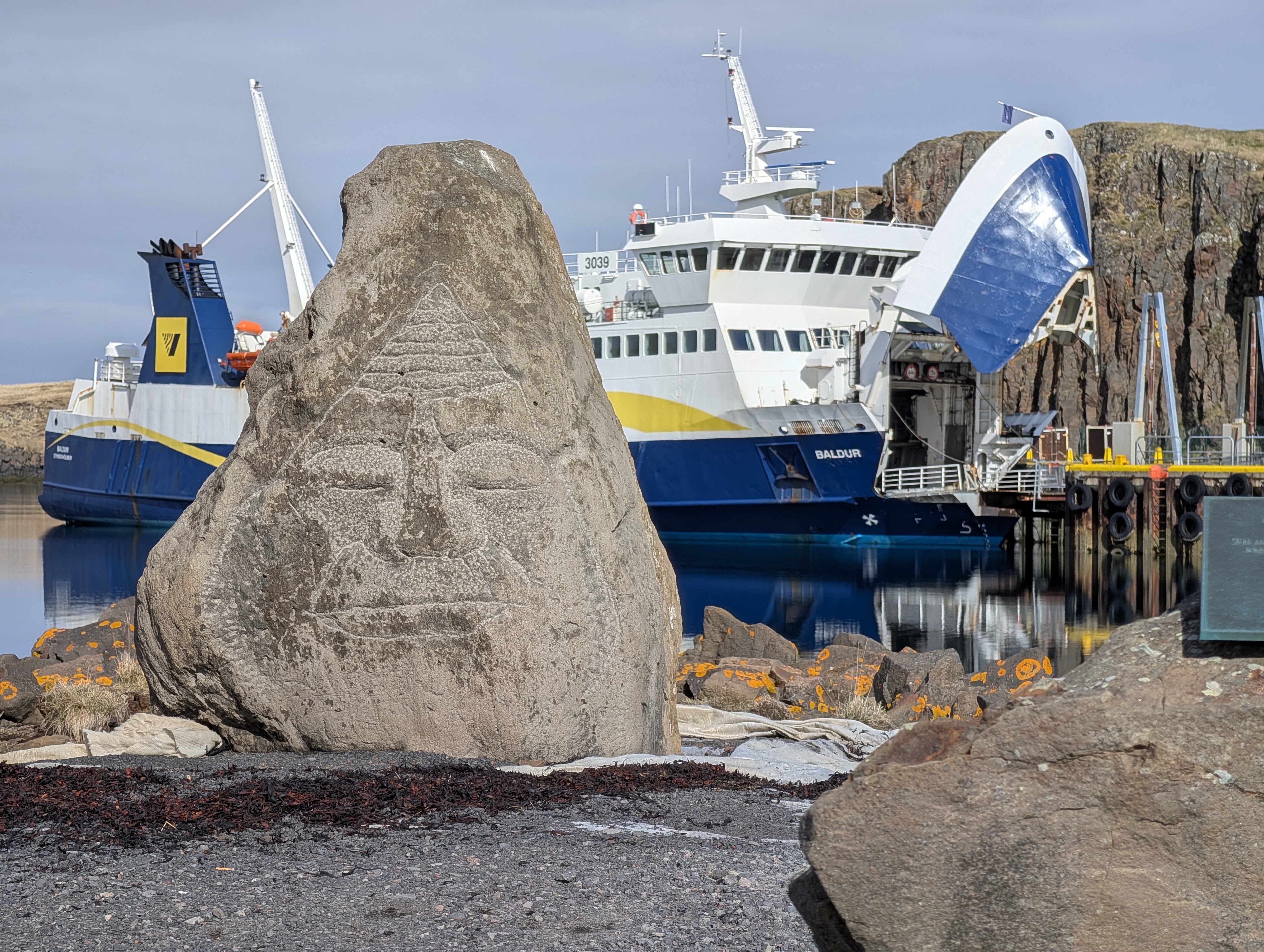 A view of a rock that has a carved face and a ship behind it.